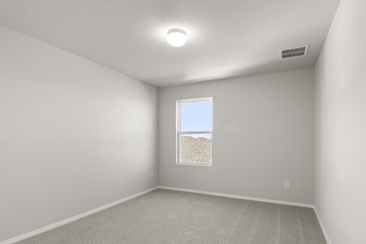 Image of a bedroom with tan carpeting, light grey walls and a window