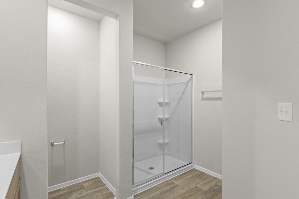 Image of a primary bathroom with beige walls, light brown wood-look flooring, and a standing shower