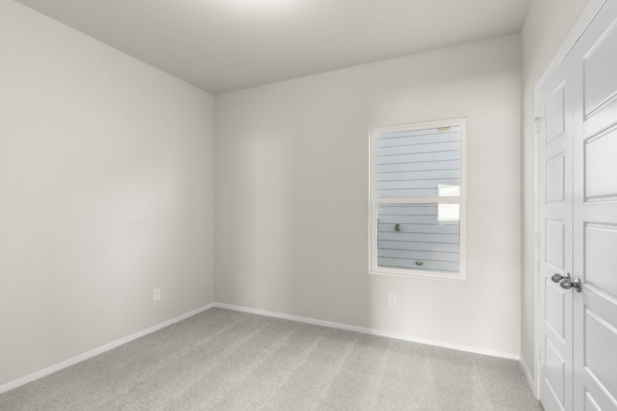 Image of a bedroom with light grey walls, tan carpeting, and a window with white trim