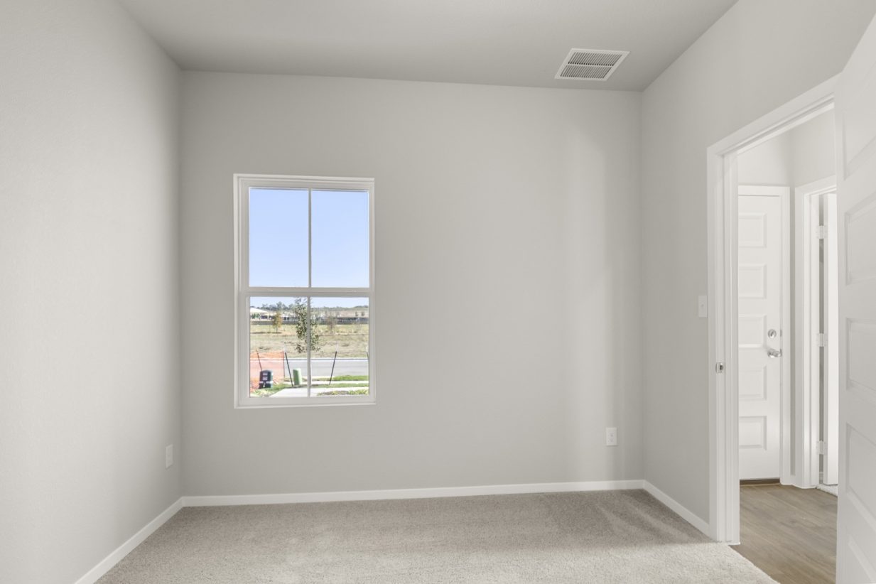 Image of a bedroom with tan carpeting, light grey walls and a window