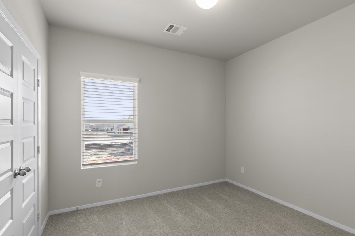 Image of a bedroom with beige walls, tan carpeting, white trim and a window with blinds