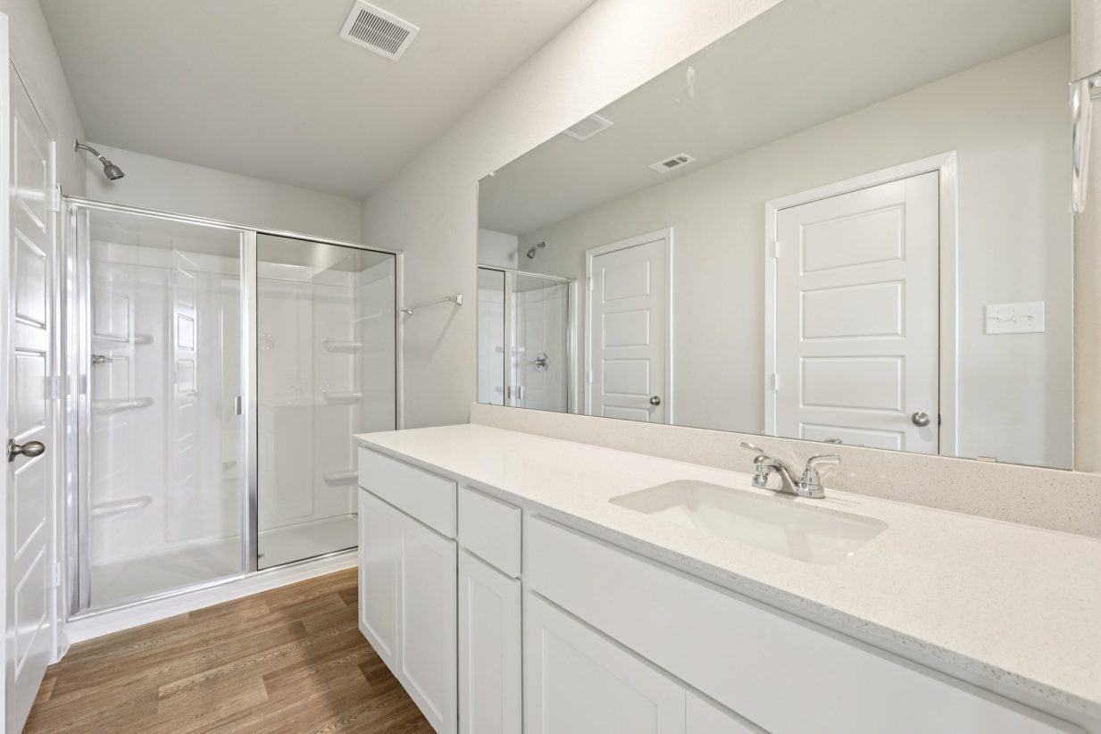 Image of a primary bathroom with a standing shower, a double white vanity, a large mirror and white cabinets