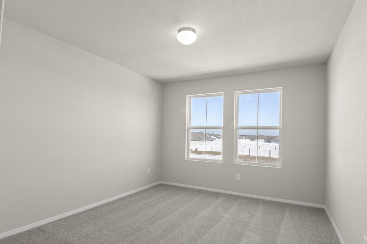 Image of a bedroom with cream walls, tan carpeting, two windows and white trim