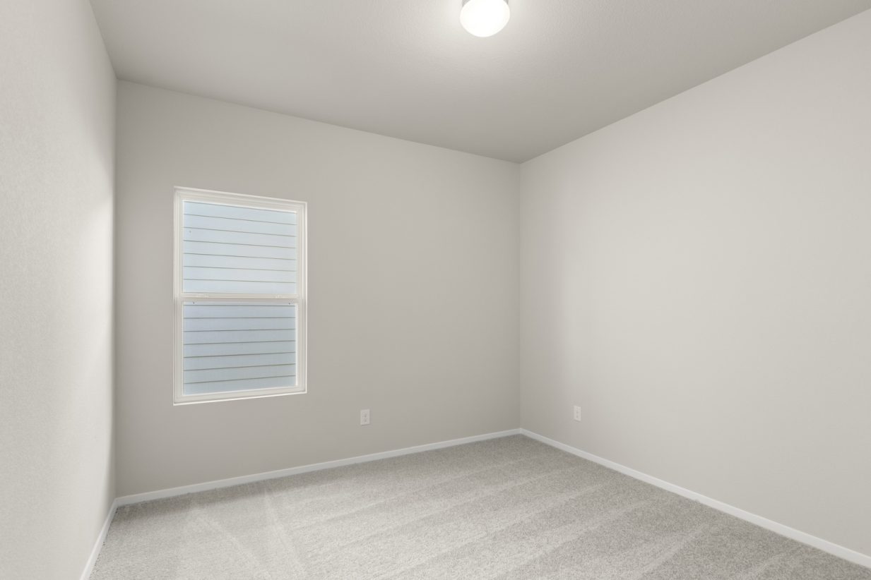 Image of a bedroom with light grey walls, tan carpeting, and a window with white trim