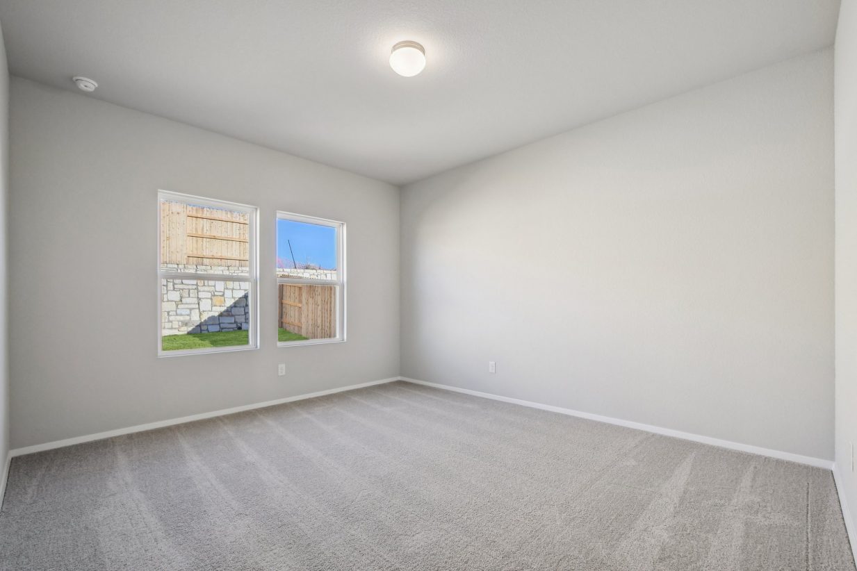 Image of a primary bedroom with light grey walls, tan carpeting, windows and white trim