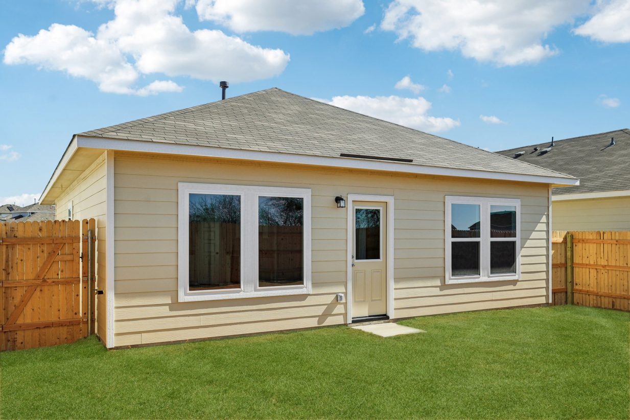 Image of the back exterior of a one story beige house with green grass and a blue sky in the background
