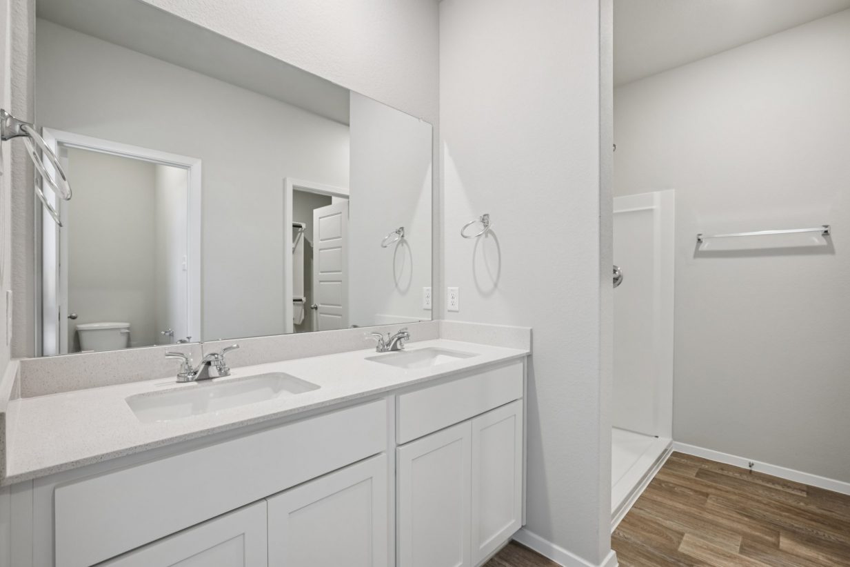 Image of a primary bathroom with white cabinets, a jack and jill vanity, a large mirror and a walk-in shower
