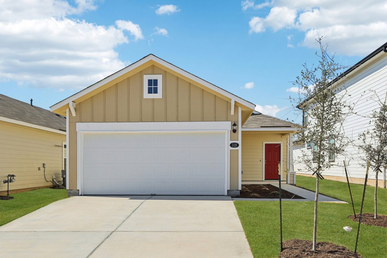 Image of a one story beige house front exterior with a red door, a white garage, a cement driveway and a blue sky in the background