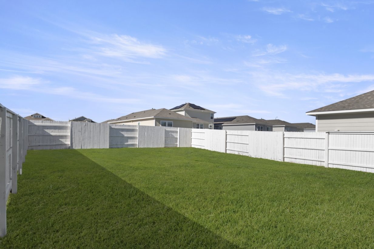 Image of a backyard with green grass, a white fence and a blue sky in the background