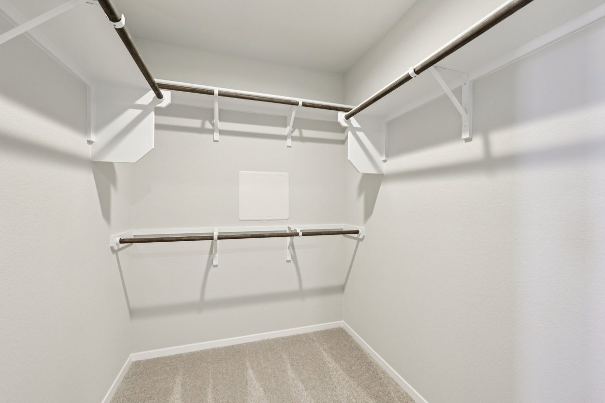 Image of a primary closet with tan carpeting and shelves