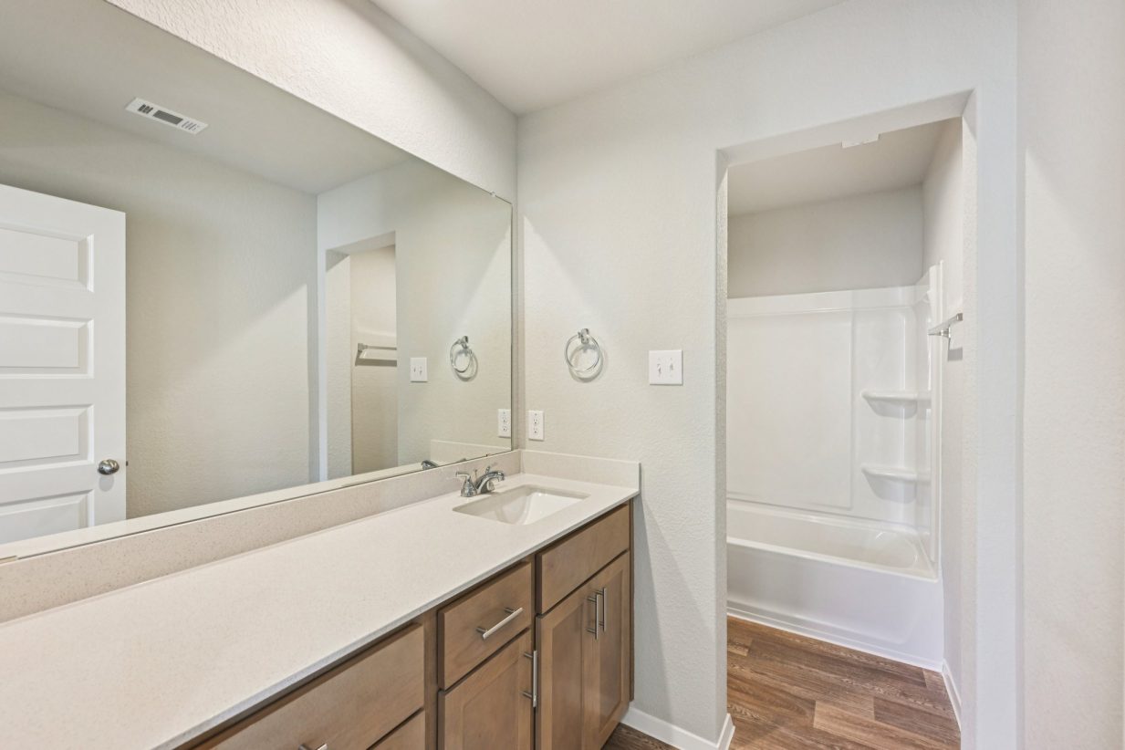 Image of a bathroom with a double vanity, brown cabinets, and a large mirror