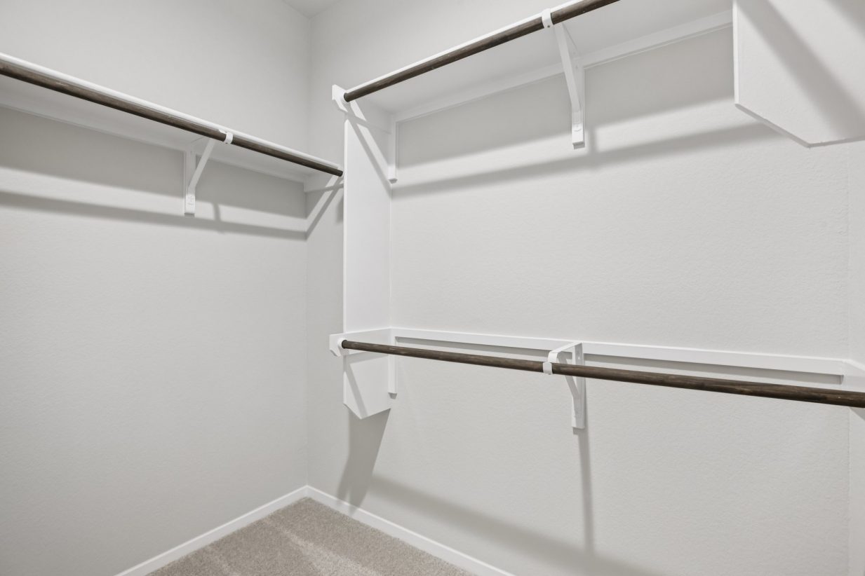 Image of a primary closet with white shelves and tan carpeting