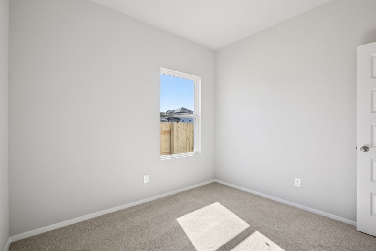 Image of a bedroom with tan carpeting, light grey walls, and a window with white trim