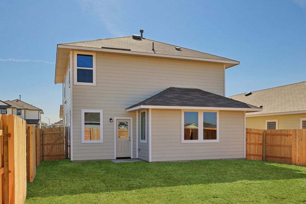 Image of the back exterior of a two story house with a wooden fence and a green grass backyard