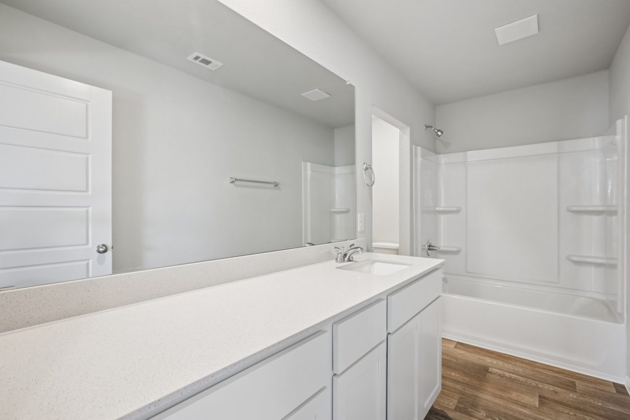 Image of a bathroom with white cabinets, a dual vanity, a large mirror, a shower with a tub, and a semi-private water closest