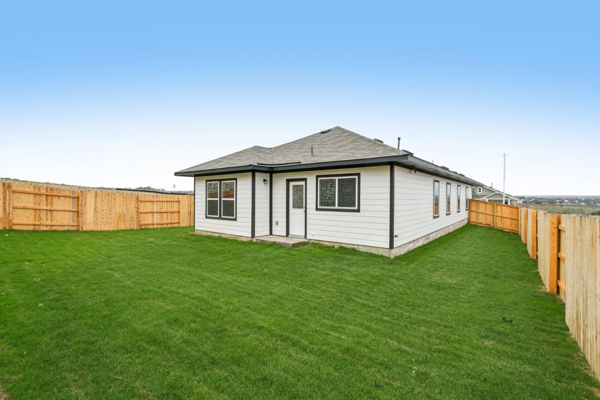 Image of a white one story house back exterior with black trim, a wooden fence and a green grass backyard