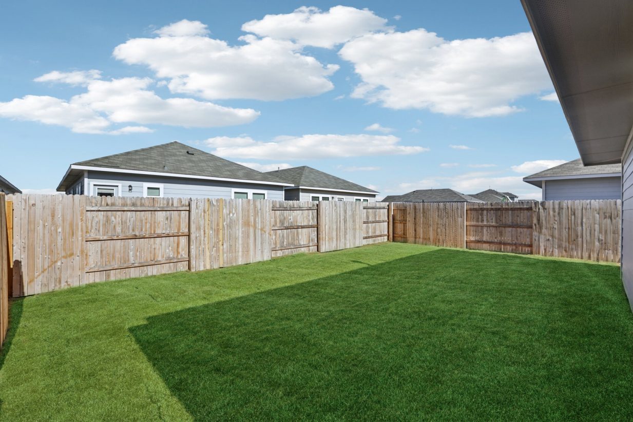 Image of a backyard with green grass, a wooden fence, and a blue sky with clouds in the background
