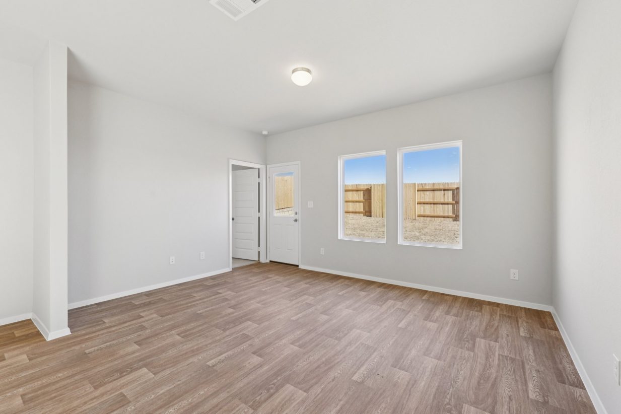 Image of a dining room with light grey walls, brown wood-look vinyl flooring, two windows and a white back door