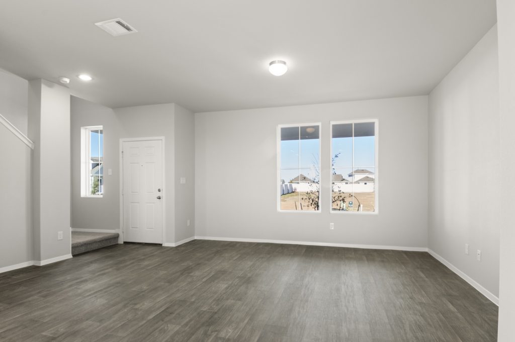 Image of a living room with dark brown vinyl flooring, light grey walls, white trim and two windows
