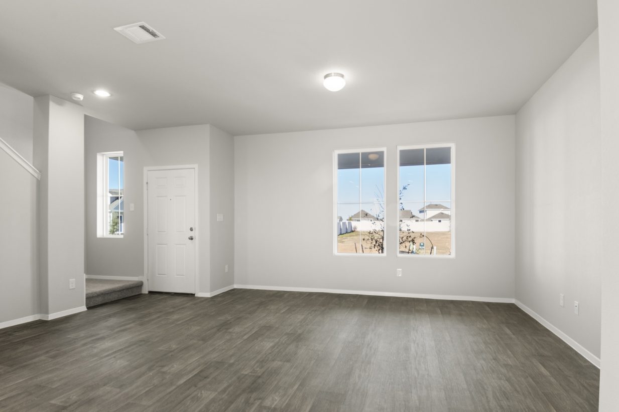 Image of a living room with dark brown vinyl flooring, light grey walls, white trim and two windows