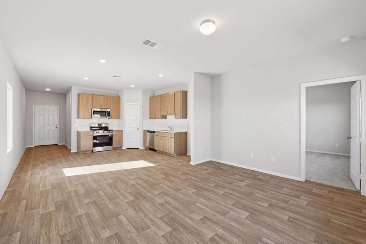 Image of a living room with light grey walls, wood-look vinyl flooring, and an open kitchen in the distance
