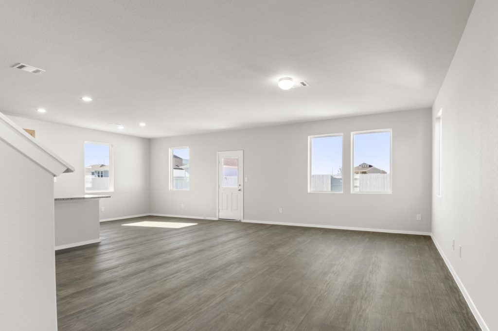 Image of a living room with brown vinyl flooring, light grey walls, and four large windows