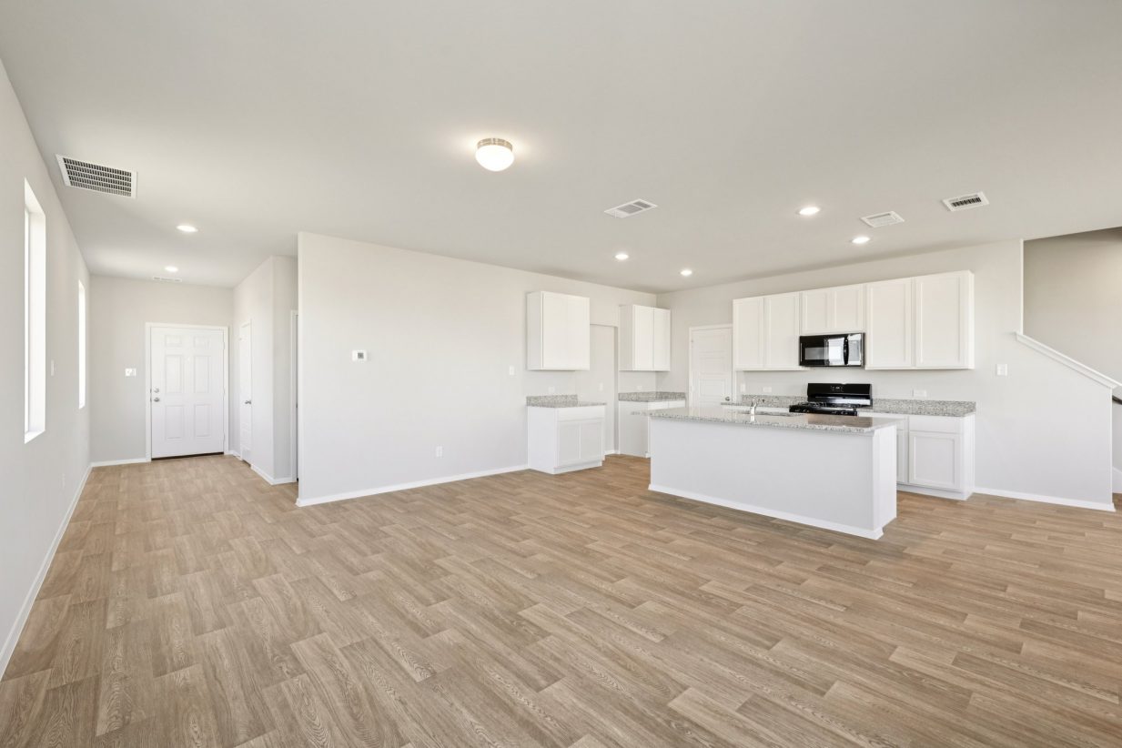 Image of a kitchen and living area with grey walls, vinyl flooring and a kitchen with white cabinets