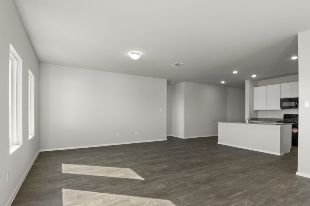 Image of a living room with light grey walls, dark brown flooring, a center island in the distance and windows