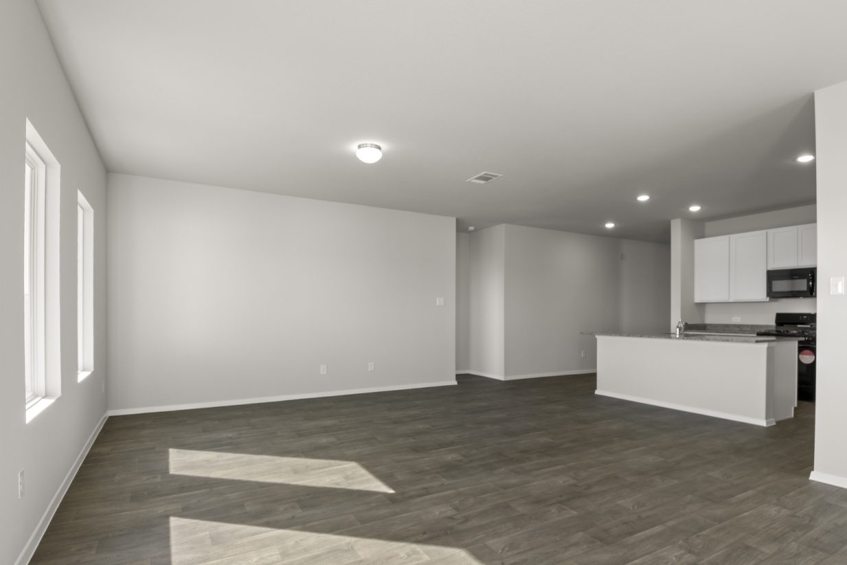 Image of a living room with light grey walls, dark brown flooring, a center island in the distance and windows