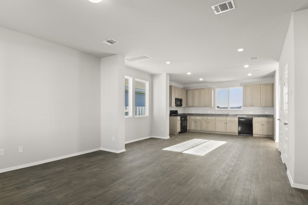 Image of a living room with dark vinyl flooring, light grey walls, and a open kitchen in the distance