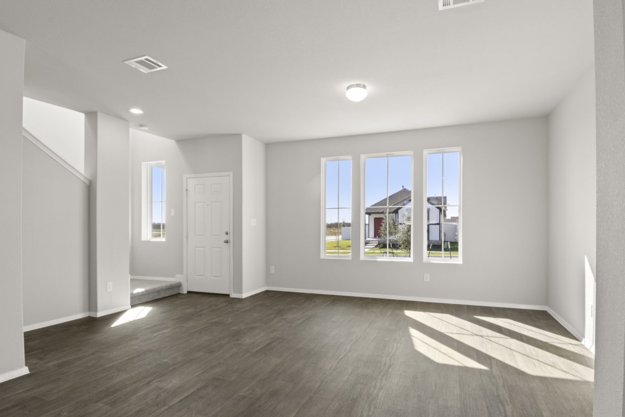 Image of a living room with light grey walls, dark brown vinyl flooring, three windows, and a staircase