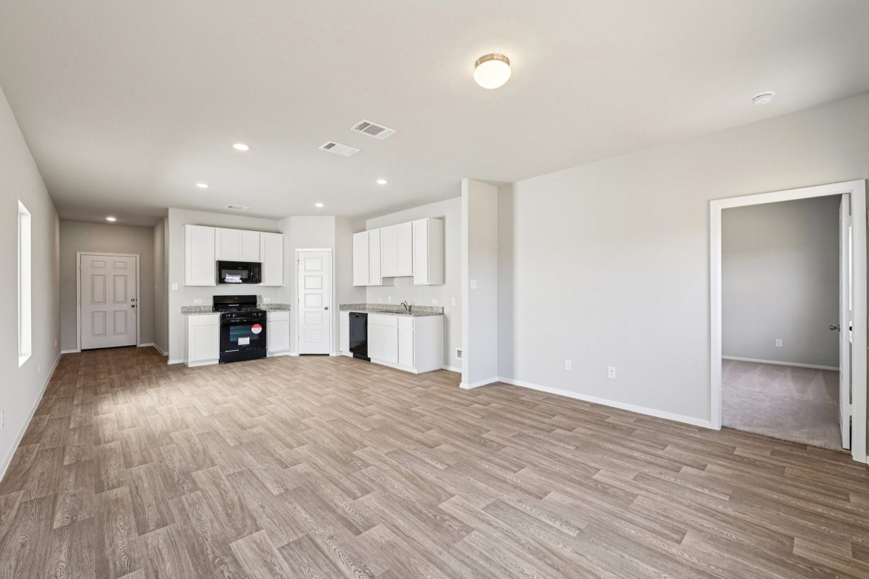 Image of a living/kitchen area with grey walls, vinyl flooring, white cabinets and black appliances