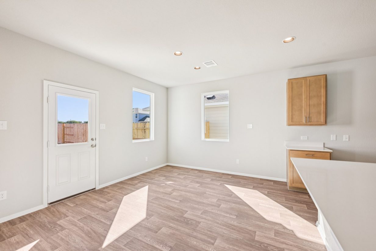 Image of a dining room area with vinyl flooring, beige walls, windows, and a back exit door