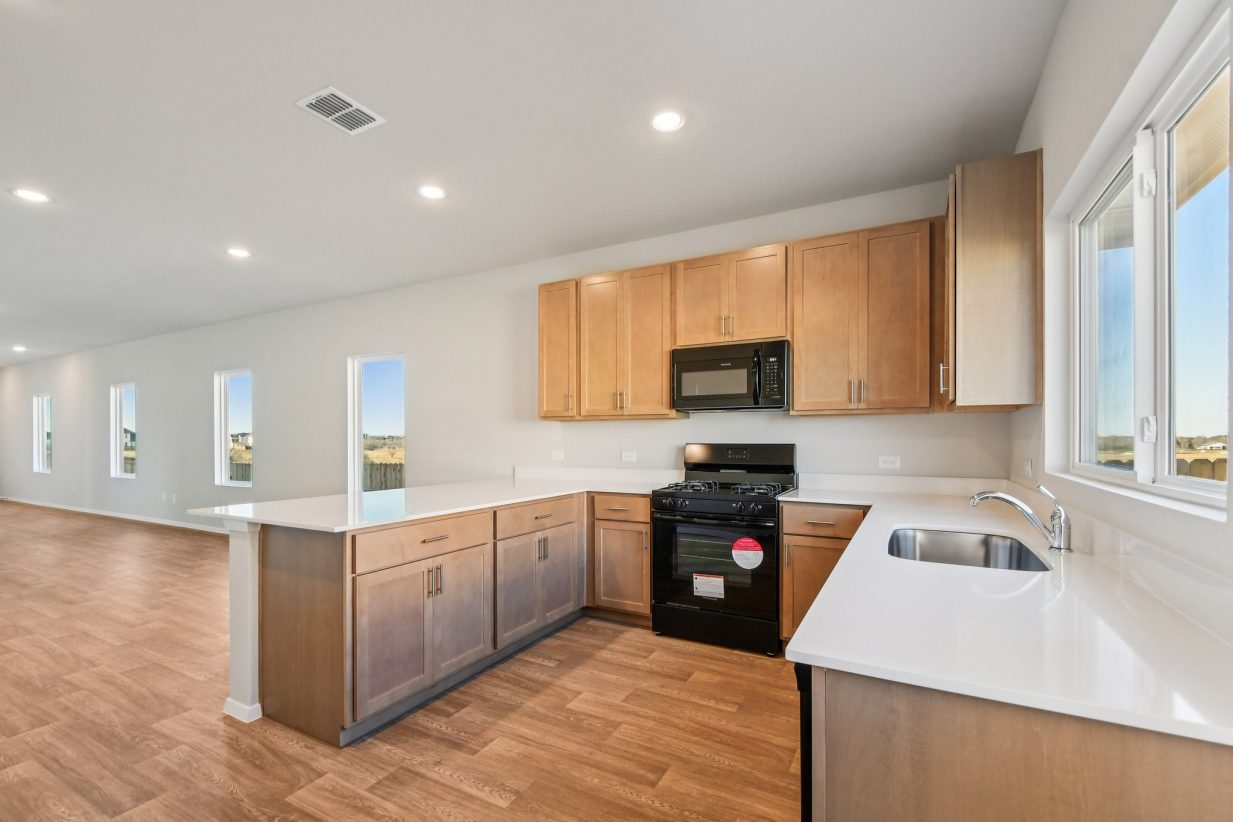 Image of a U-shaped kitchen with brown cabinets, white countertops, black appliances and a window above the sink