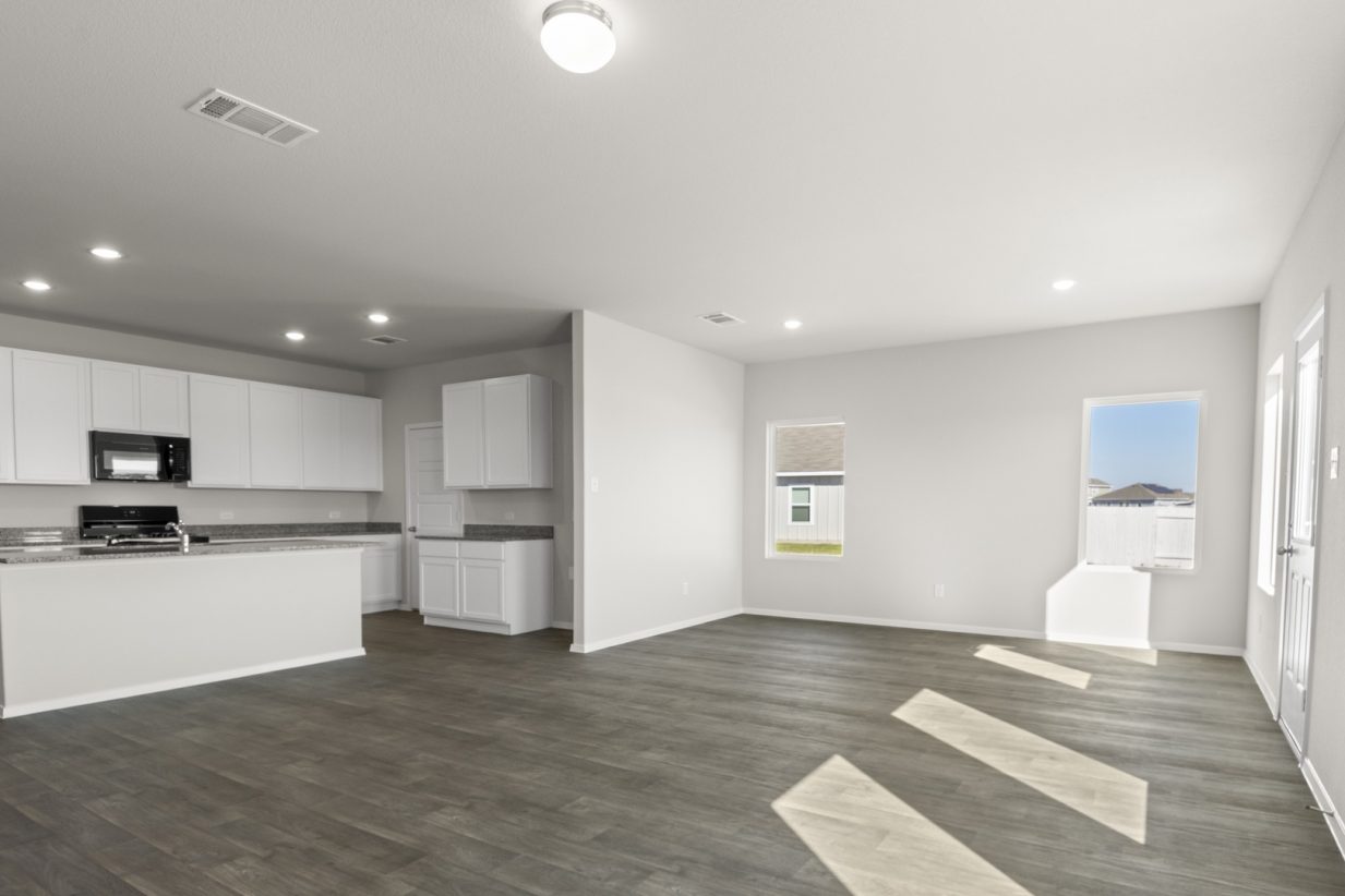 Image of a living room with light grey walls, dark brown walls, windows, white trim and an open kitchen to the left