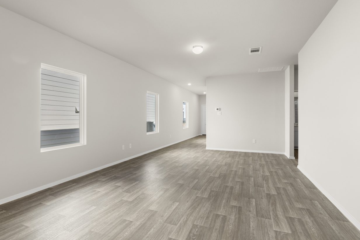 Image of a living room with beige walls, brown wood-look flooring, white trim, and windows