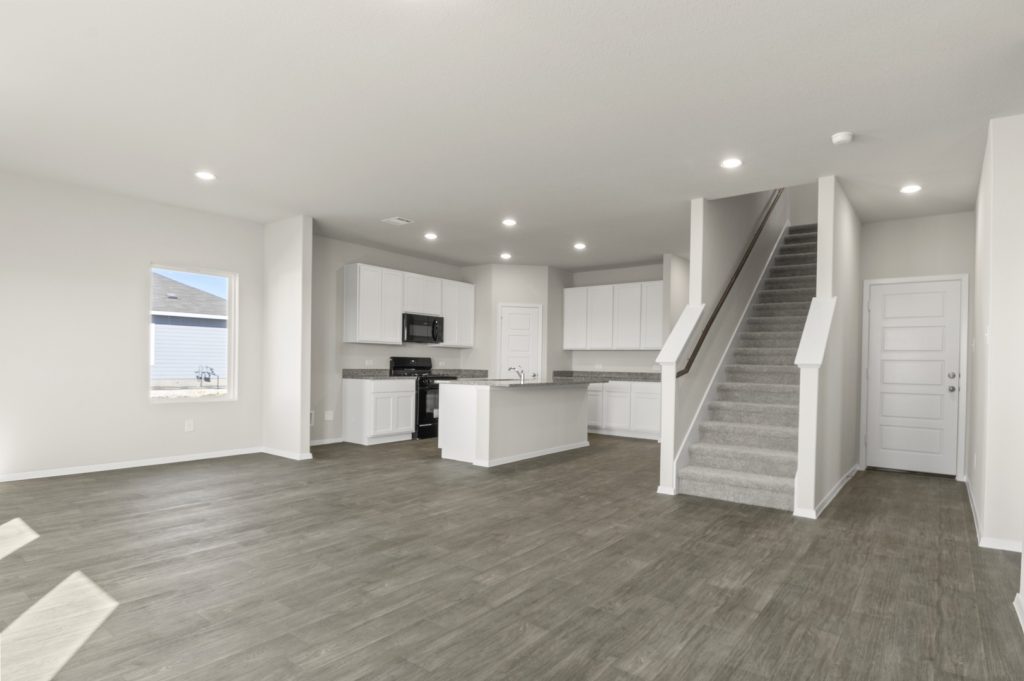 Image of a living room with cream walls, dark brown flooring, an open layout kitchen and a staircase that leads updtairs