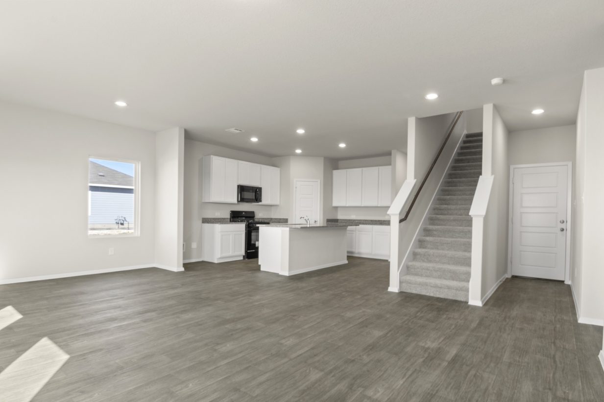 Image of a living room with cream walls, dark brown flooring, an open layout kitchen and a staircase that leads updtairs