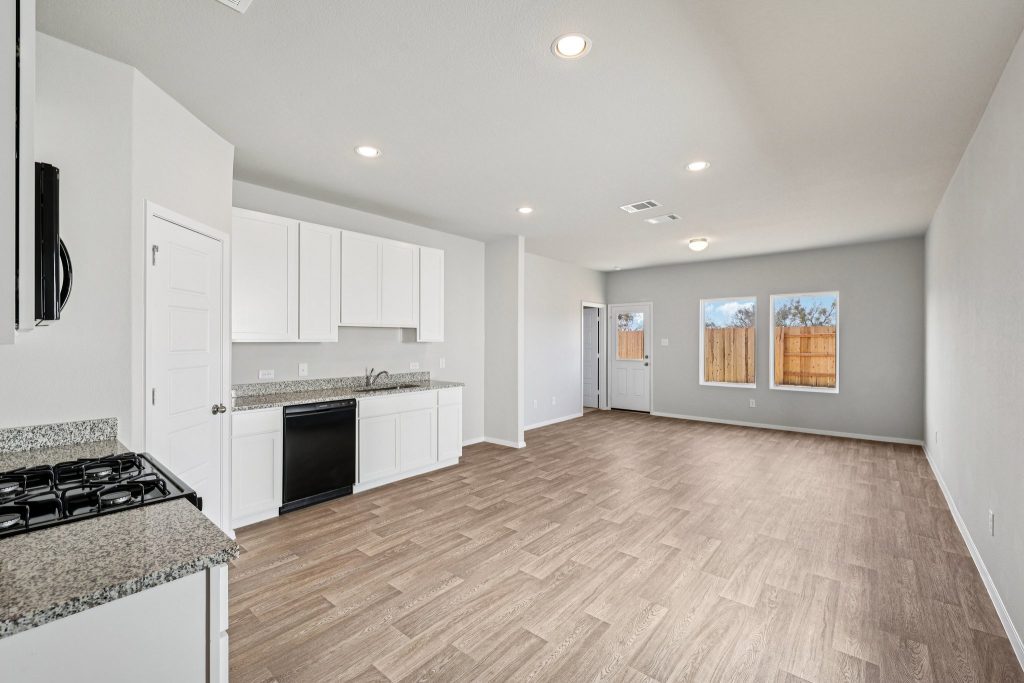Image of a kitchen and living area with white cabinets, vinyl flooring, windows and white trim
