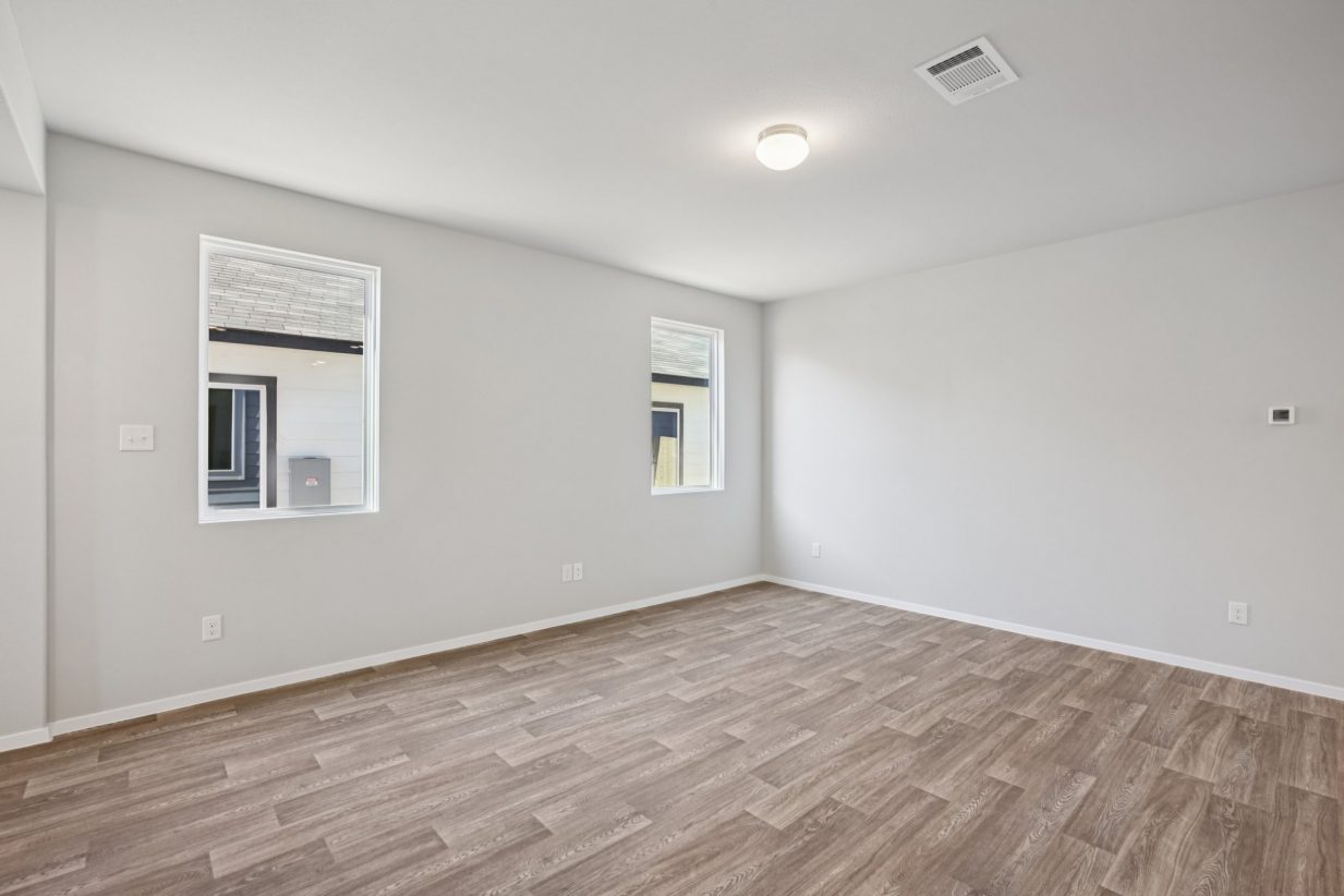 Image of a living room with light grey walls, brown wood-look flooring, two windows and white trim