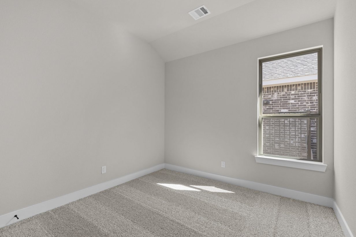 Image of a bedroom with beige walls, tan carpeting and a brown window with tan trim