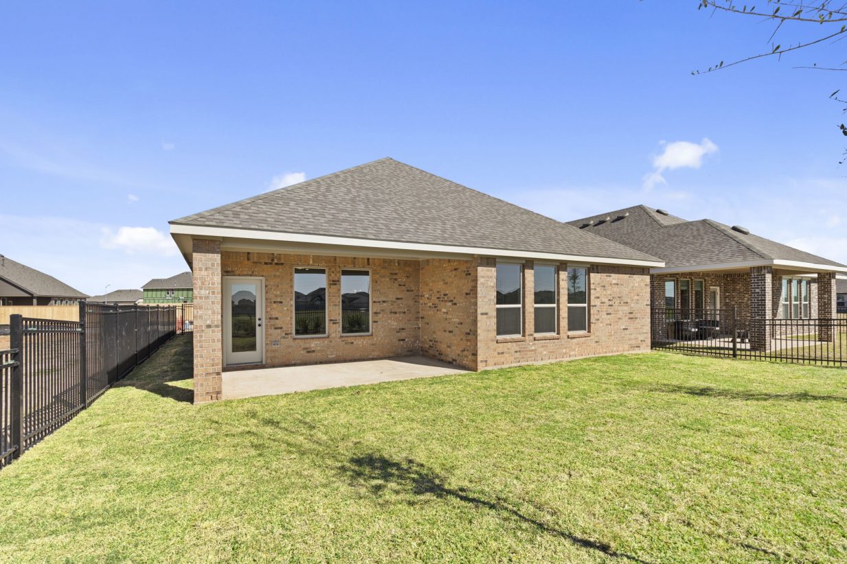 Image of a back exterior of a brick one story home with green grass and a blue sky in the background