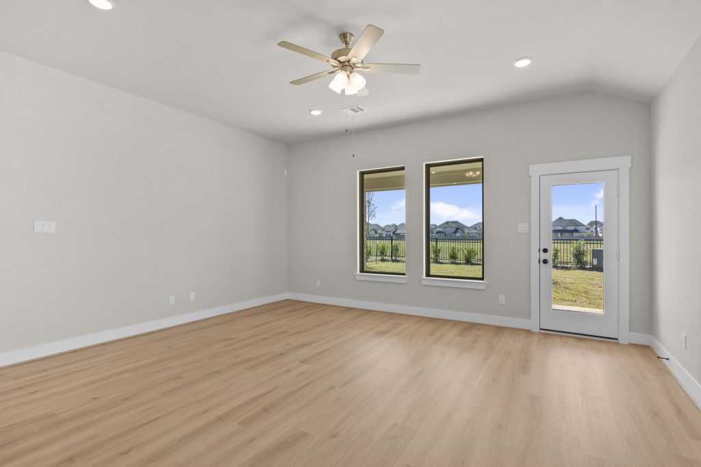 Image of a living room with beige walls, light brown floors, windows and a ceiling fan
