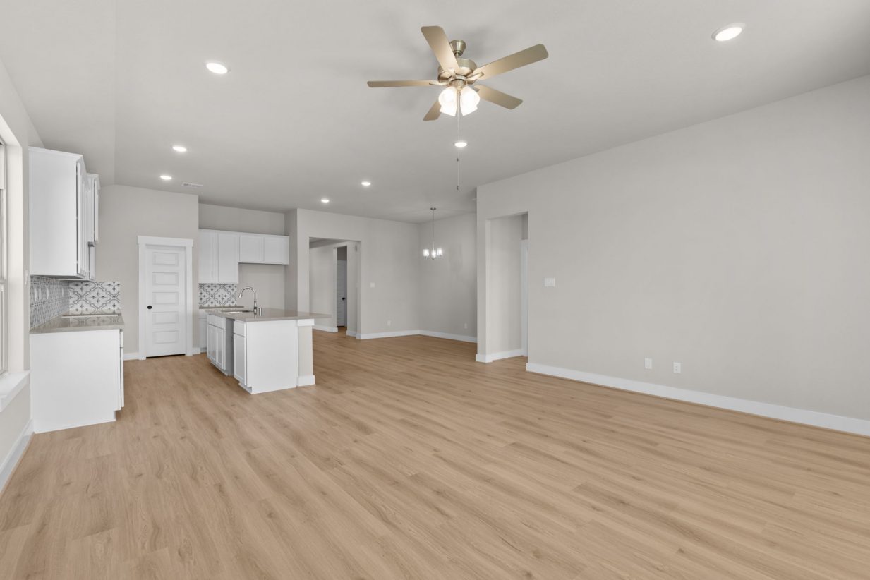 Image of a living room with tan walls, light brown floors and a ceiling fan