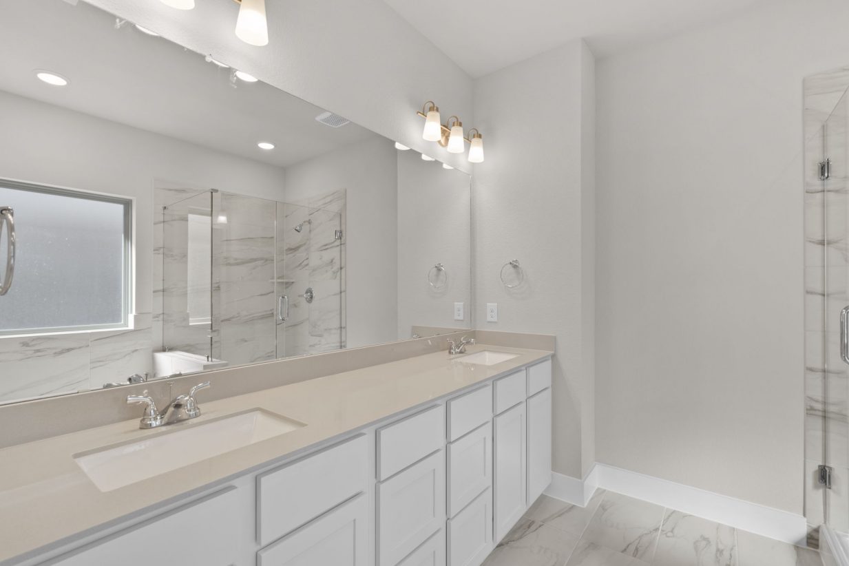Image of a primary bathroom with a double vanity, a large mirror and white cabinets