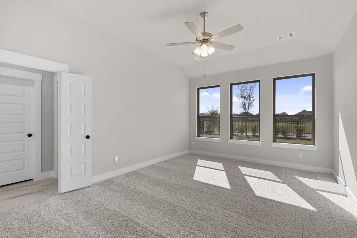 Image of a primary bedroom with beige walls, tan carpeting, and three windows
