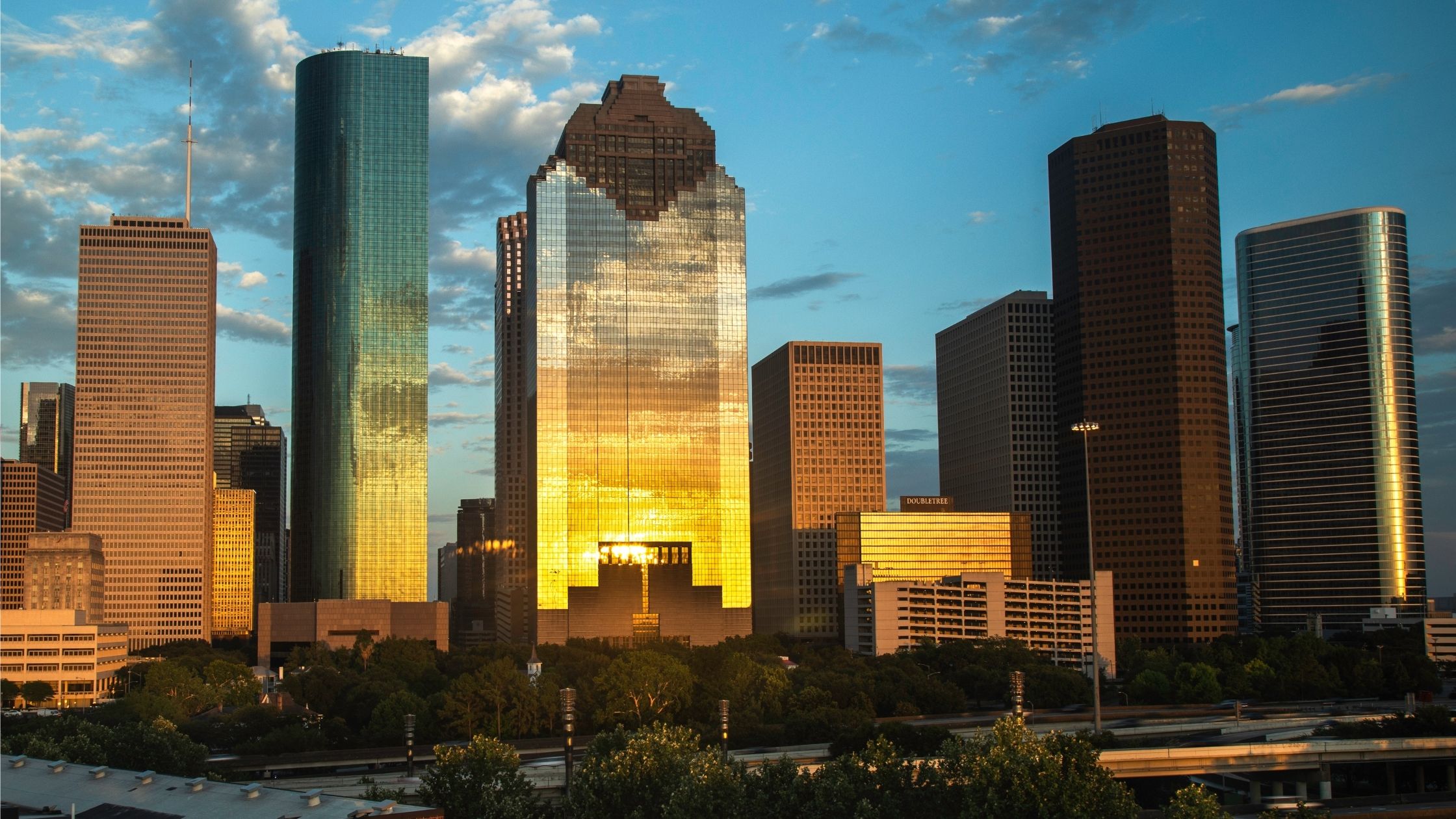 Image of the Houston city skyline at sunset with a blue sky with clouds in the background.