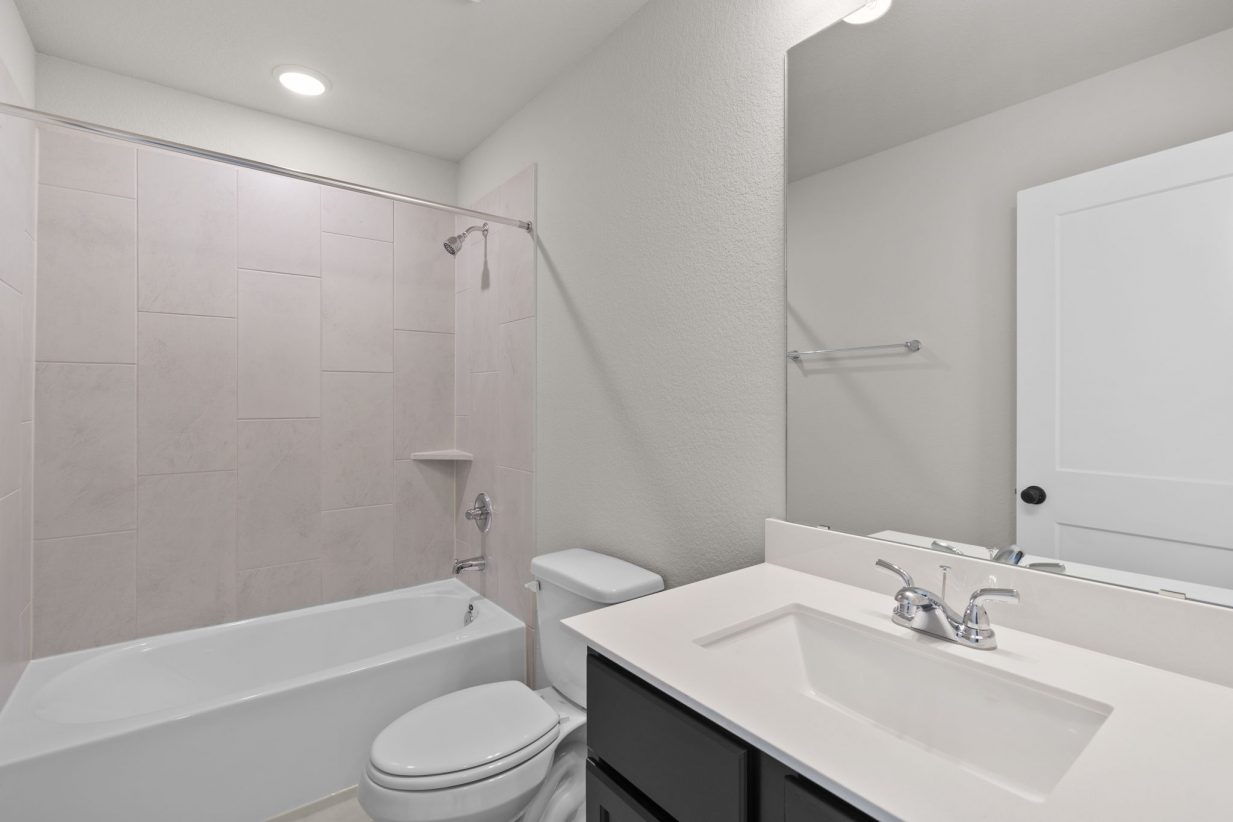 Image of a bathroom with a white vanity, black cabinets, a mirror and a shower with tan tiles