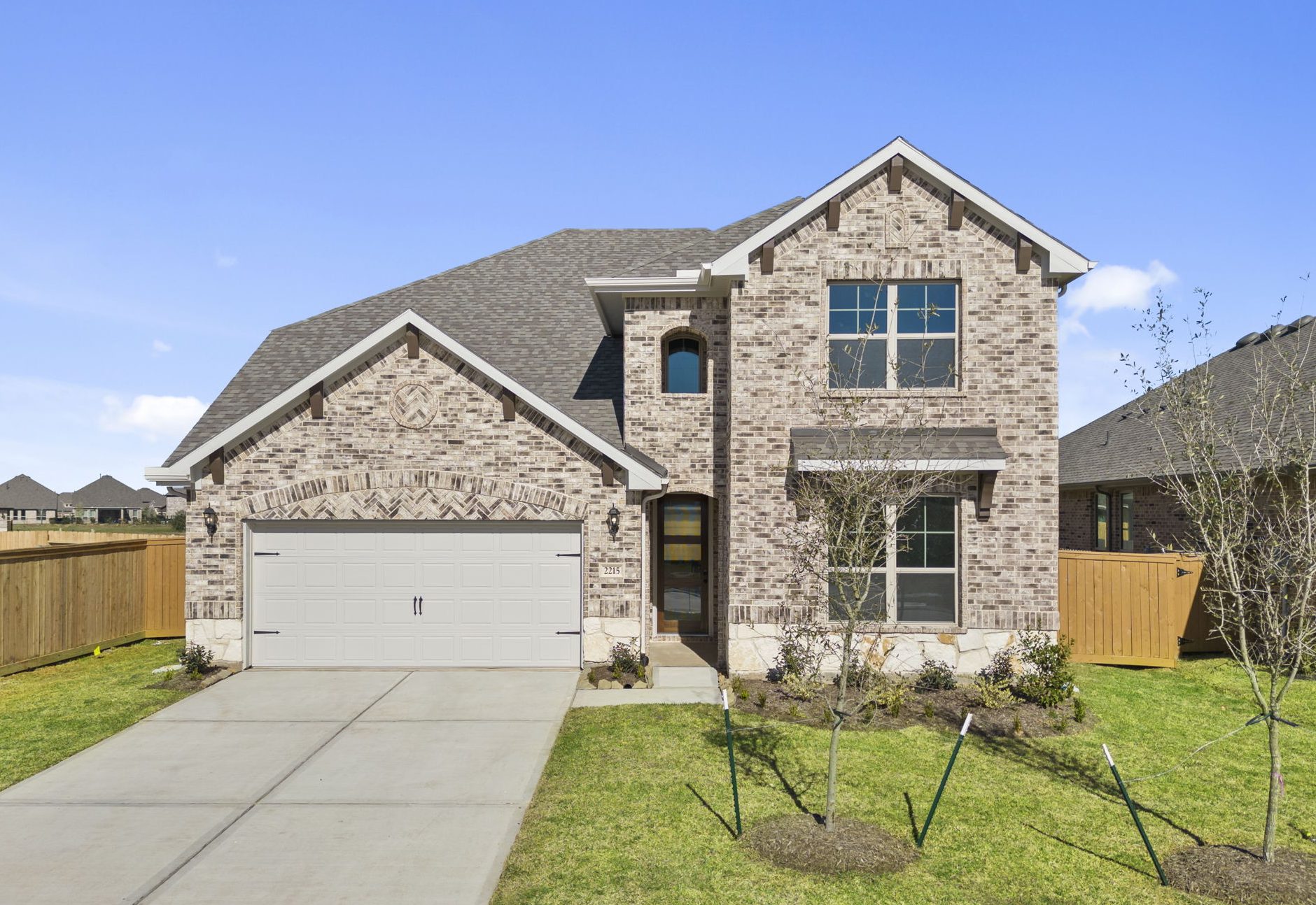 Image of a two story brick home with a white garage, green grass and a blue sky