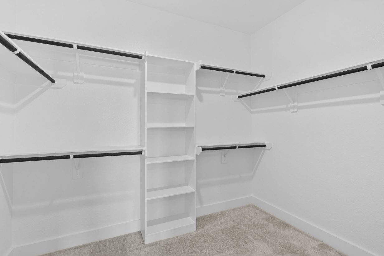 Image of a primary closet with white shelves and tan carpeting